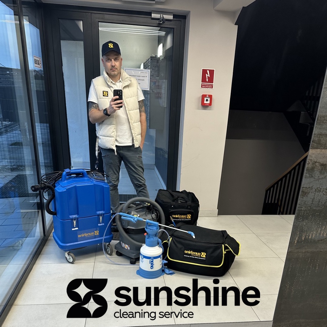 Pracownik z telefonem i sprzęt do czyszczenia tapicerki: niebieski odkurzacz piorący, odkurzacz przemysłowy i torby z akcesoriami na tle klatki schodowej.