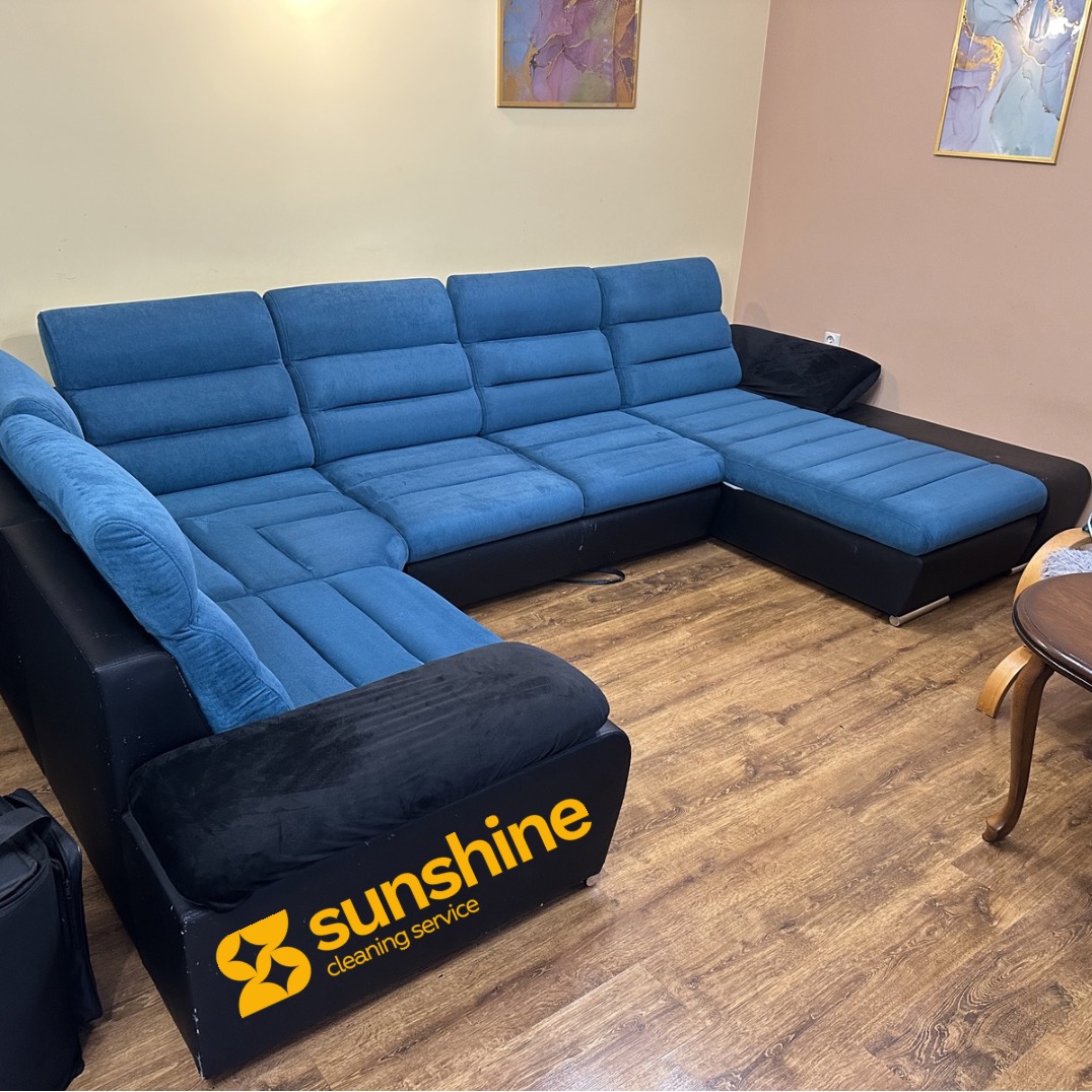 Narożnik z niebieską tapicerką i czarnymi bokami, z logo firmy sprzątającej 'Sunshine cleaning service' na boku. Ustawiony na drewnianej podłodze.