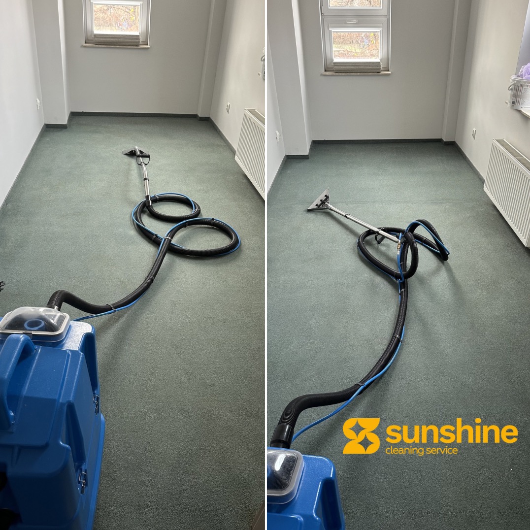 Profesjonalne urządzenie do czyszczenia dywanów na zielonej wykładzinie w jasnym pomieszczeniu z oknem. Widoczny fragment logo firmy sprzątającej.