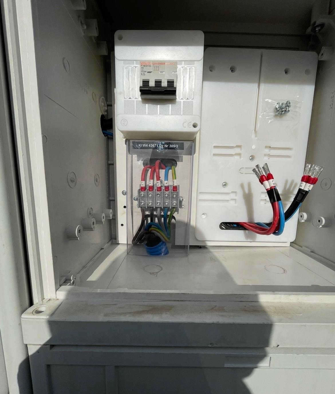 Wnętrze skrzynki elektrycznej z zamontowanym licznikiem i zabezpieczeniami. Widoczne przewody z końcówkami tulejkowymi. Nowa instalacja w białej obudowie.