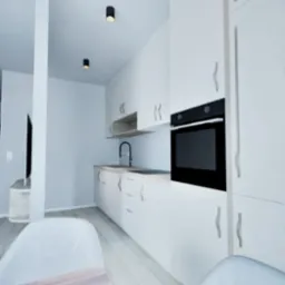 Wizualizacja nowoczesnej kuchni z białymi szafkami, czarnym piekarnikiem i drewnianym blatem stołu. Minimalistyczny design, jasne wnętrze.