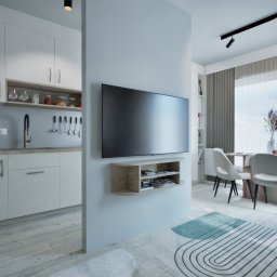 To Oni Projektują - Nowoczesne wnętrze: minimalistyczna kuchnia z białymi szafkami, telewizor na ścianie oddzielającej od jadalni z oknem i krzesłami w jasnych barwach.