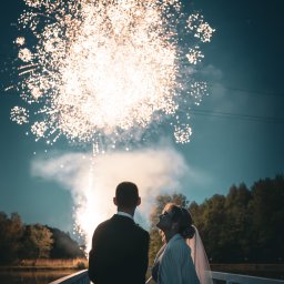 Michał Wawerek Fotografia - Para młoda wpatruje się w fajerwerki na tle nocnego nieba, stojąc na białym moście. Romantyczna sceneria ślubna z delikatnym oświetleniem.