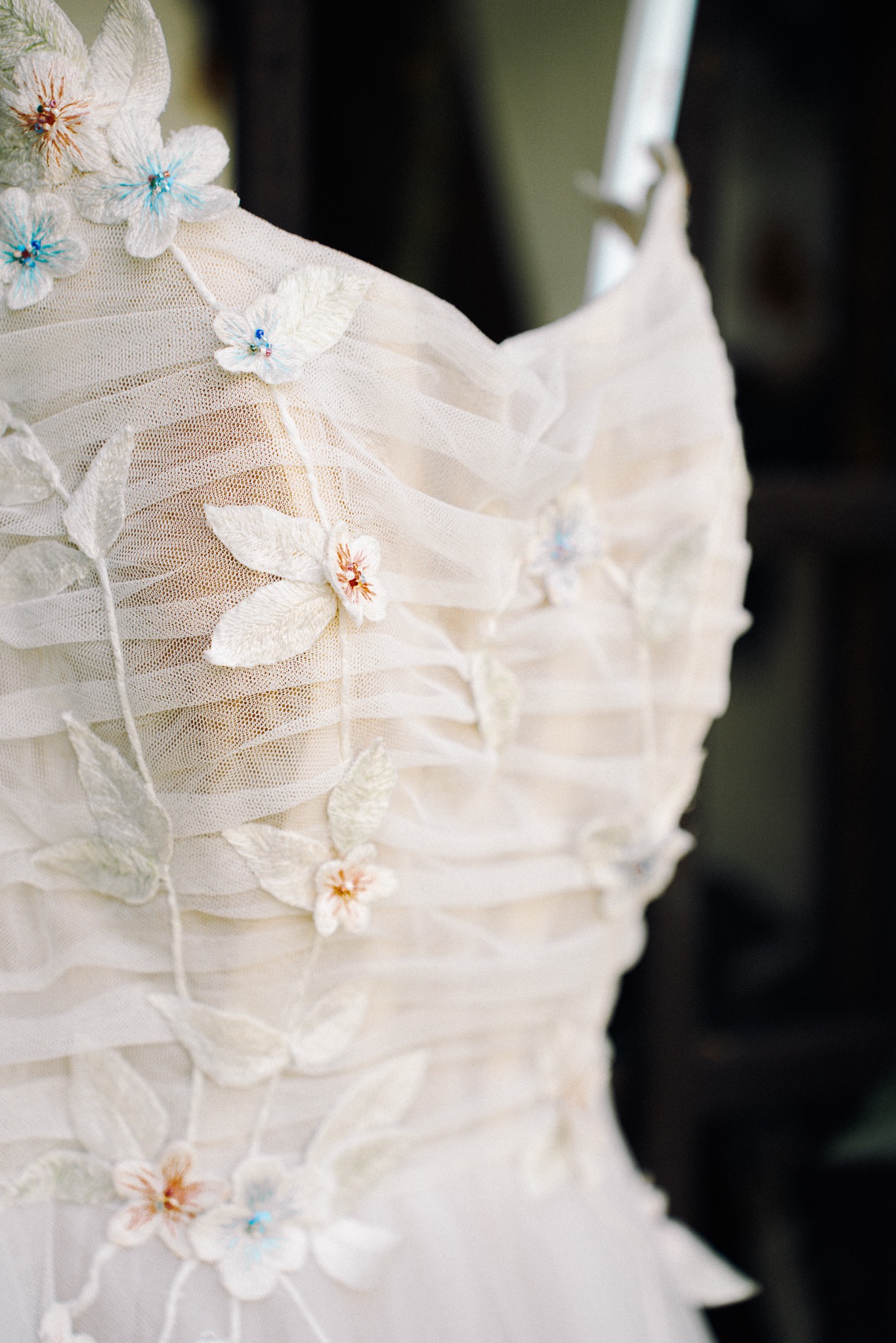 Delikatna suknia ślubna z koronkowymi aplikacjami kwiatowymi w odcieniach bieli i błękitu, z bliska, ukazująca detale i fakturę materiału.