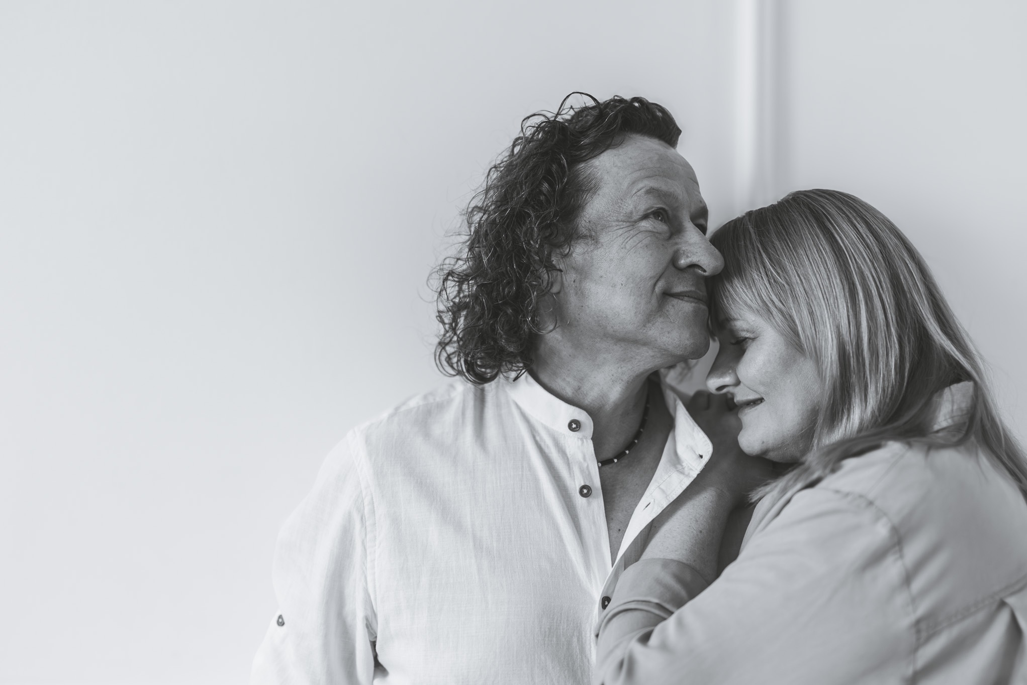 Czarno-białe, intymne zbliżenie pary w Bydgoszczy: mężczyzna z kręconymi włosami i kobieta z blond włosami, przytuleni policzkami, wyrażający bliskość i ciepło.