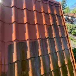 Częściowo wyczyszczony, czerwony dach z dachówki ceramicznej, widoczne różnice w kolorze i czystości. Połowa dachu umyta, druga pokryta mchem i zabrudzeniami.