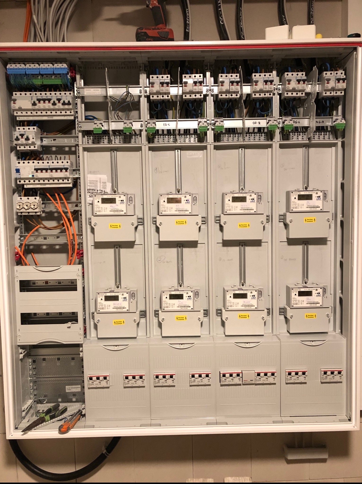 Rozdzielnia elektryczna z zamontowanymi licznikami, zabezpieczeniami i okablowaniem. Widoczne narzędzia elektryczne w dolnej części szafy.