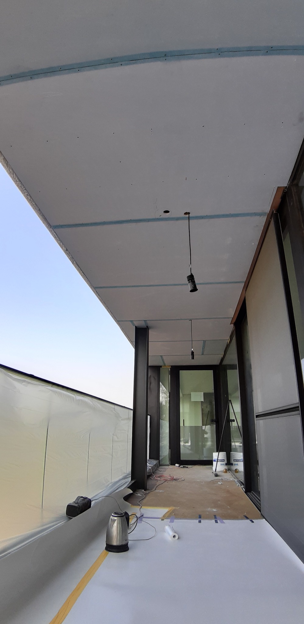 Montaż płyt karton-gips na suficie z widocznymi profilami, przygotowane podłoże i wiszące lampy. Widoczne narzędzia pracy i zabezpieczenia.