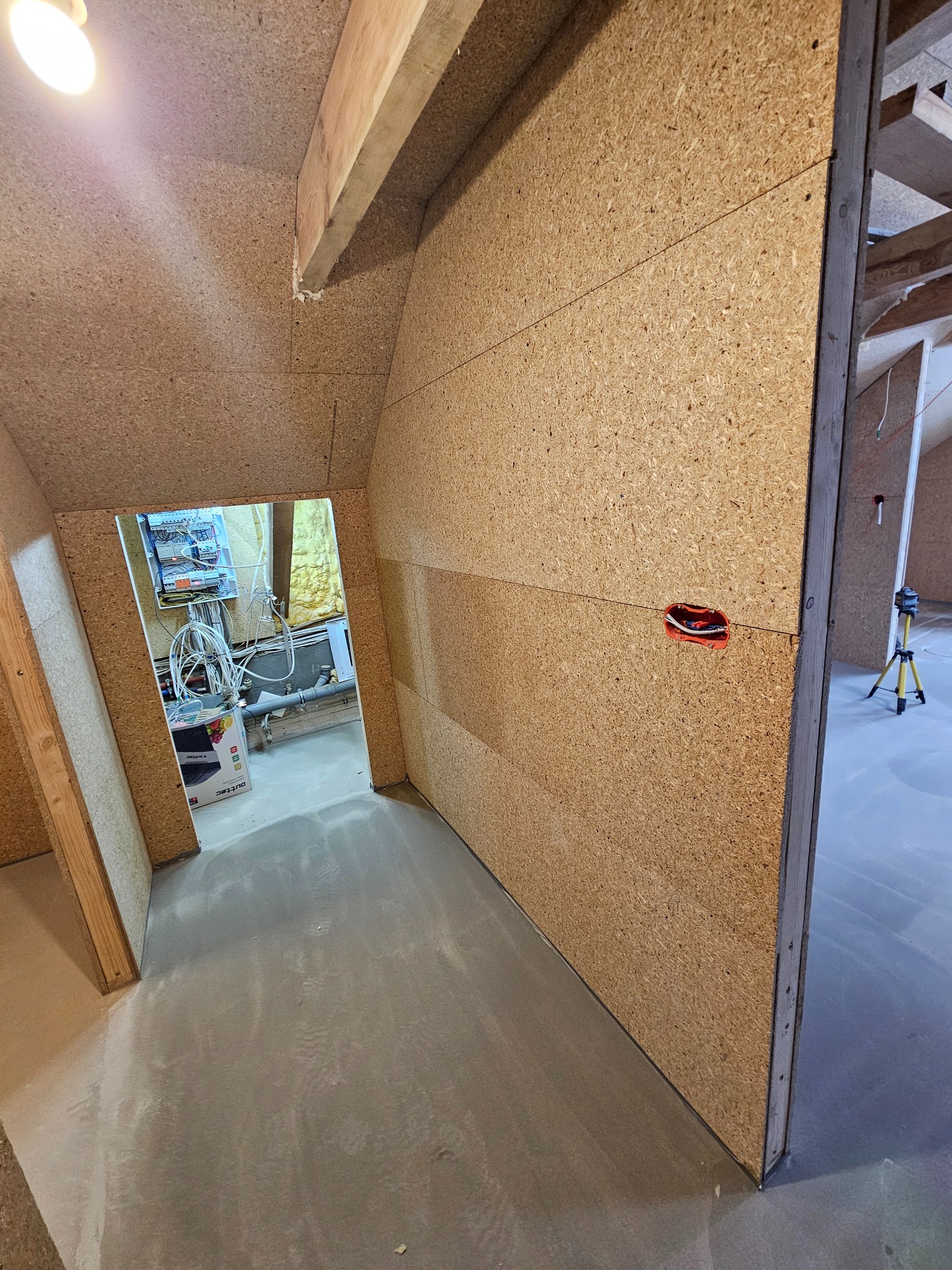 Montaż płyt OSB na poddaszu, widoczne kable elektryczne w puszce, poziomica laserowa w tle. Surowy stan wykończenia, przygotowanie do dalszych prac.