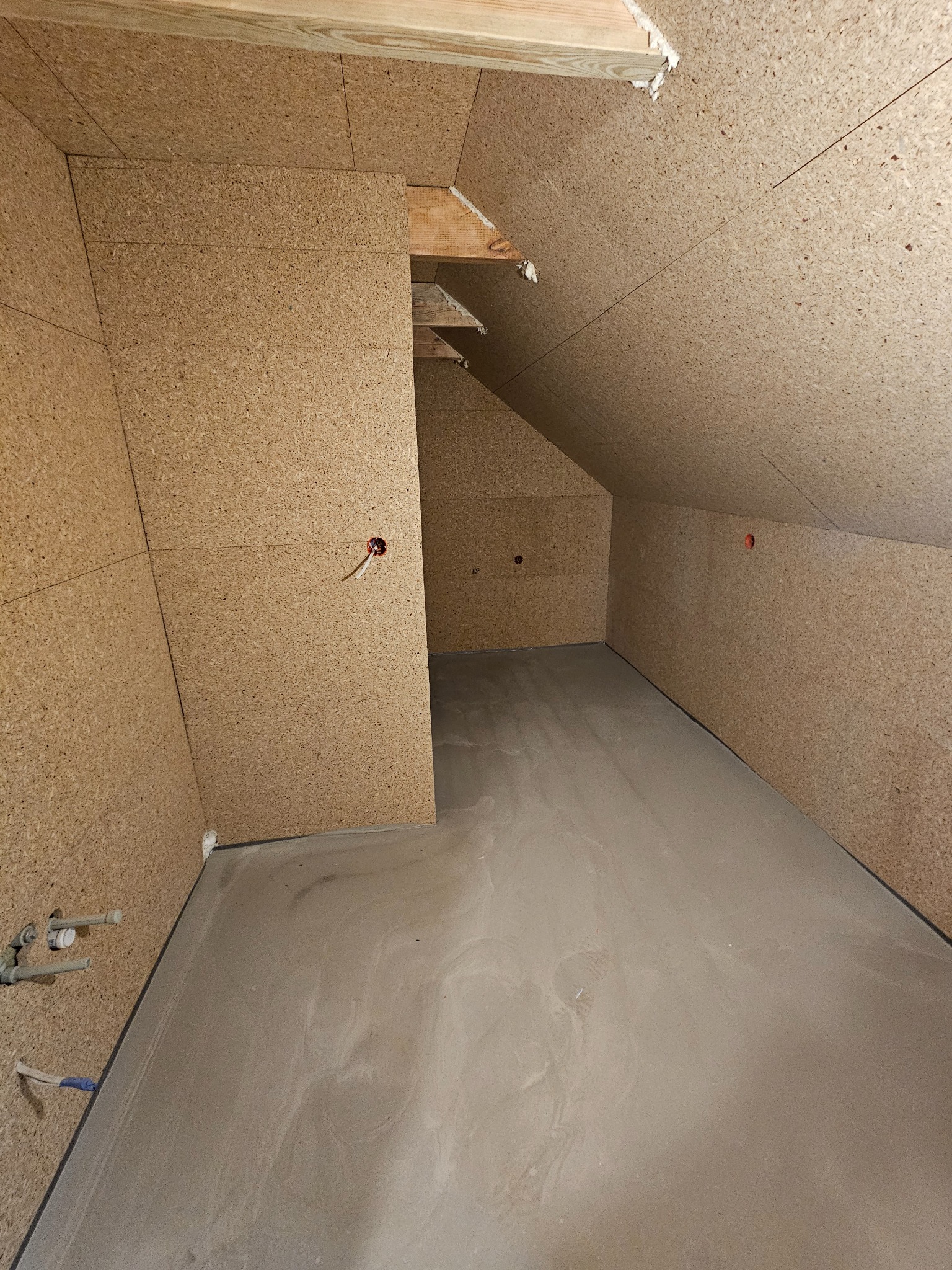 Poddasze wykończone płytami OSB, widoczne instalacje elektryczne i hydrauliczne. Surowy stan przed dalszymi pracami wykończeniowymi.