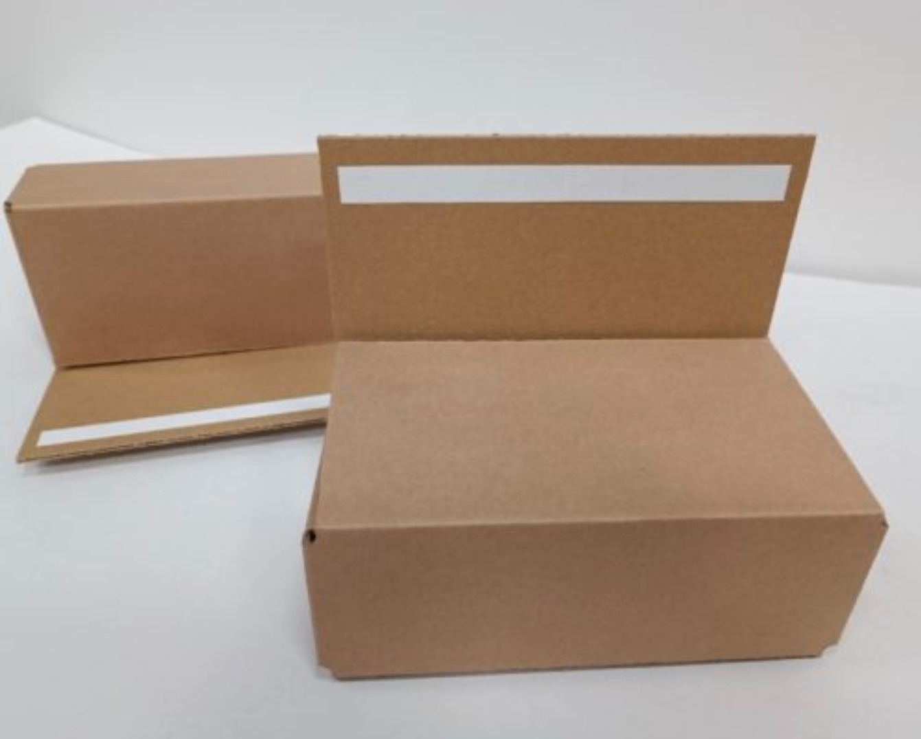 Dwa otwarte, tekturowe pudełka z paskami kleju, ukazujące proces przygotowania do pakowania. Neutralne tło, bliskie ujęcie.