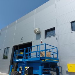 FHU KlimArt ARTUR KOPYTKO - Montaż klimatyzacji na elewacji budynku przemysłowego z użyciem podnośnika koszowego. Widoczny klimatyzator, okna i skrzynki gazowe.