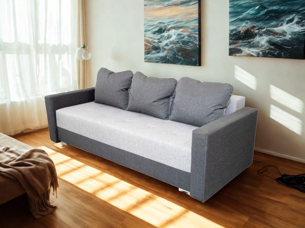 Rozłożona sofa z szarymi poduszkami i bokami na drewnianej podłodze, oświetlona promieniami słońca wpadającymi przez okno z firankami.