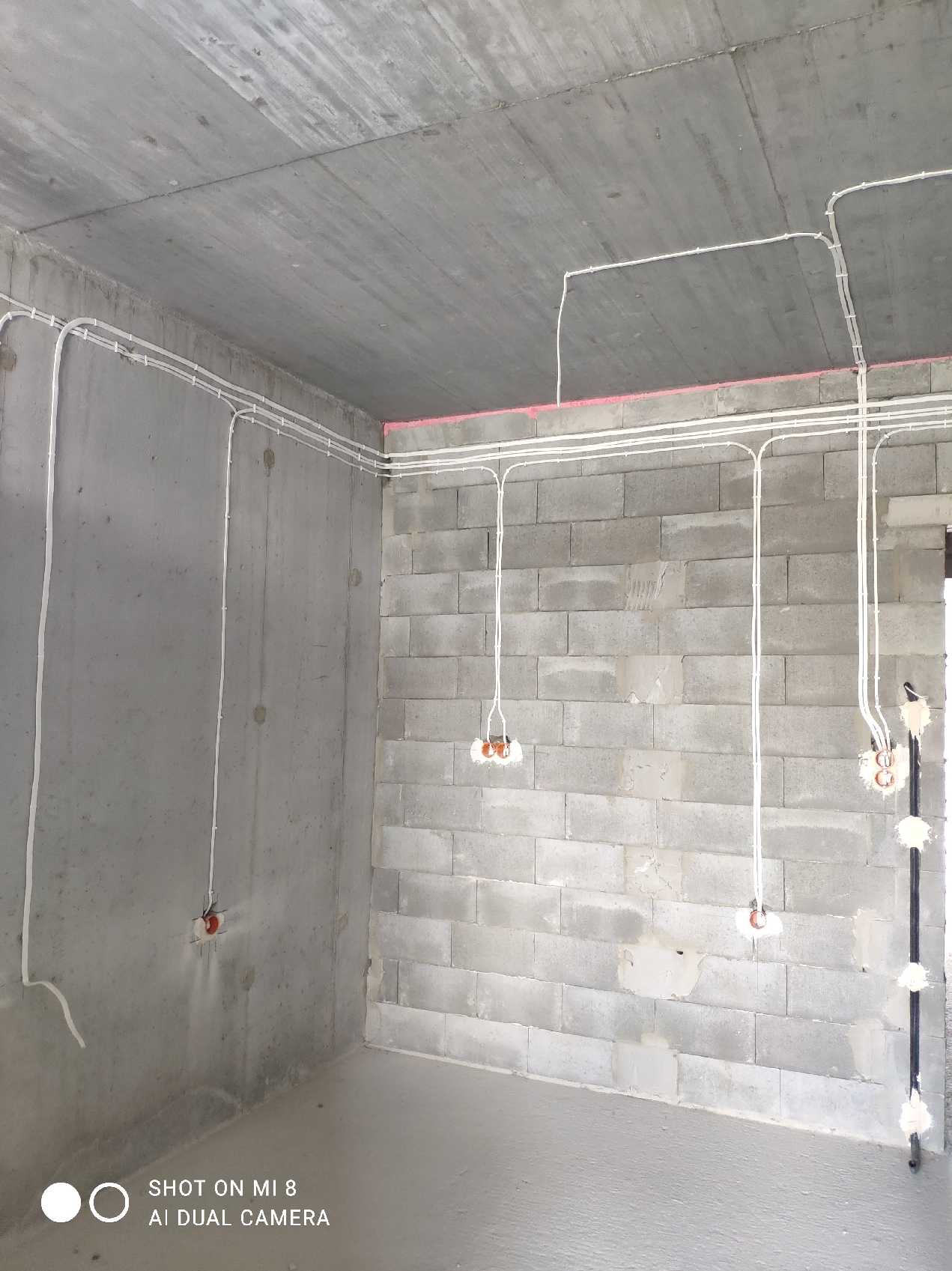 Surowy stan: białe kable elektryczne ułożone na ścianach z betonu komórkowego i suficie, widoczne puszki instalacyjne, brak osprzętu.