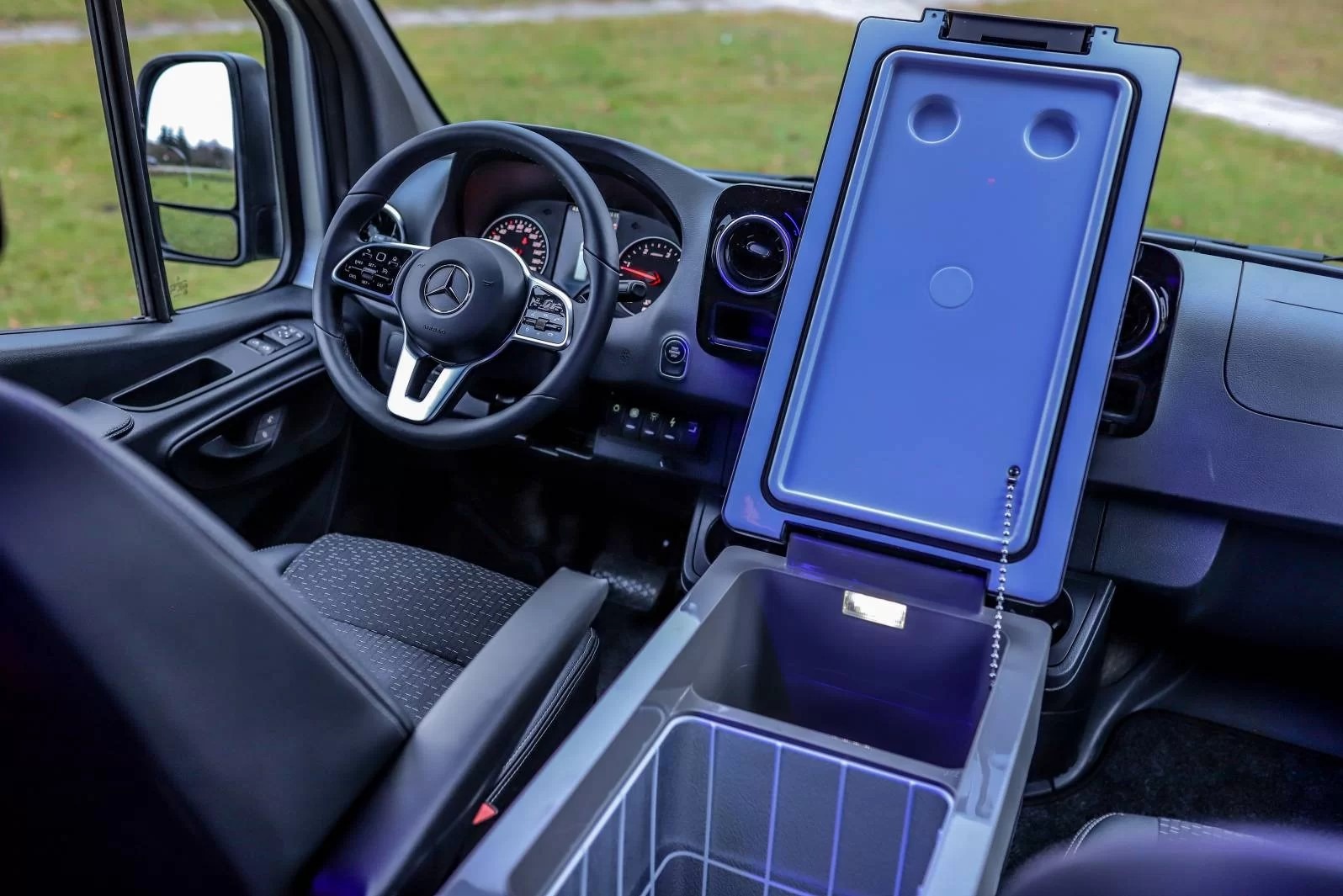 Wnętrze busa Mercedes z chłodziarką turystyczną. Widoczne fotele, kierownica z logo, deska rozdzielcza i otwarty pojemnik chłodzący. Oświetlenie LED wewnątrz.