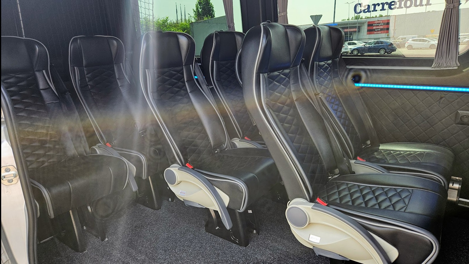 Wnętrze luksusowego busa z czarnymi, skórzanymi fotelami z pikowaniem w romby, podświetleniem LED i widokiem na Carrefour w Katowicach.