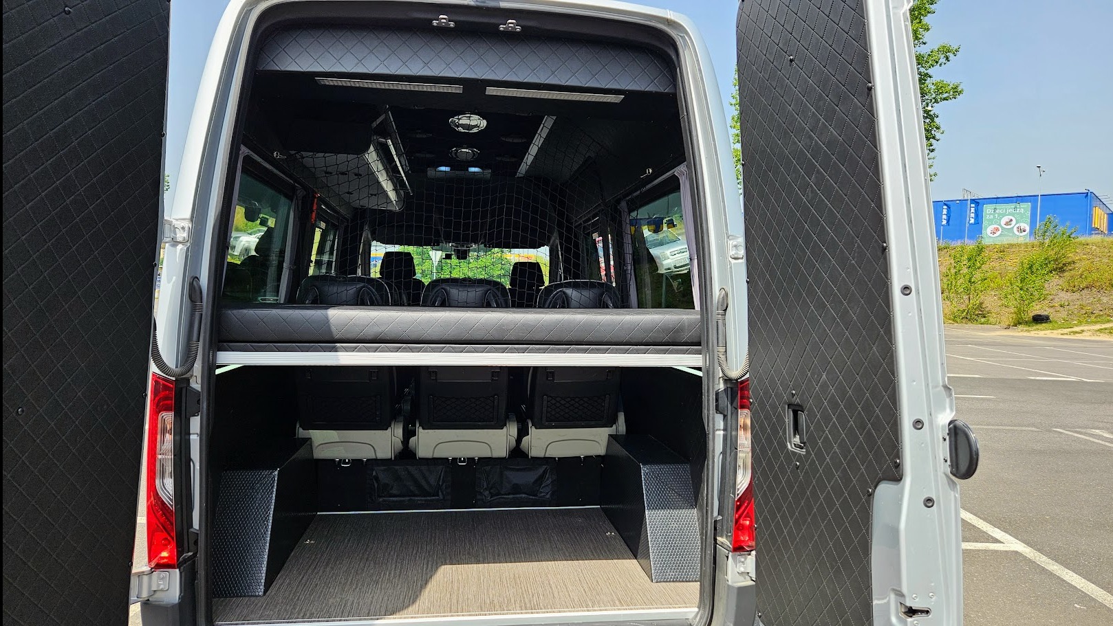 Wnętrze luksusowego busa z otwartymi drzwiami, widok z tyłu. Skórzane wykończenie, siatka zabezpieczająca bagaż, oświetlenie sufitowe. Wyjątkowy komfort podróży.