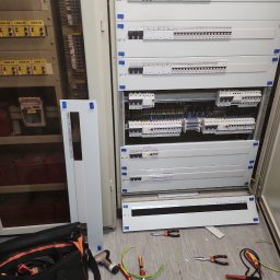 3xNC elektro - Rozdzielnica elektryczna w trakcie montażu: widoczne kable, narzędzia i elementy instalacji elektrycznej. Otwarta szafa z bezpiecznikami i okablowaniem.