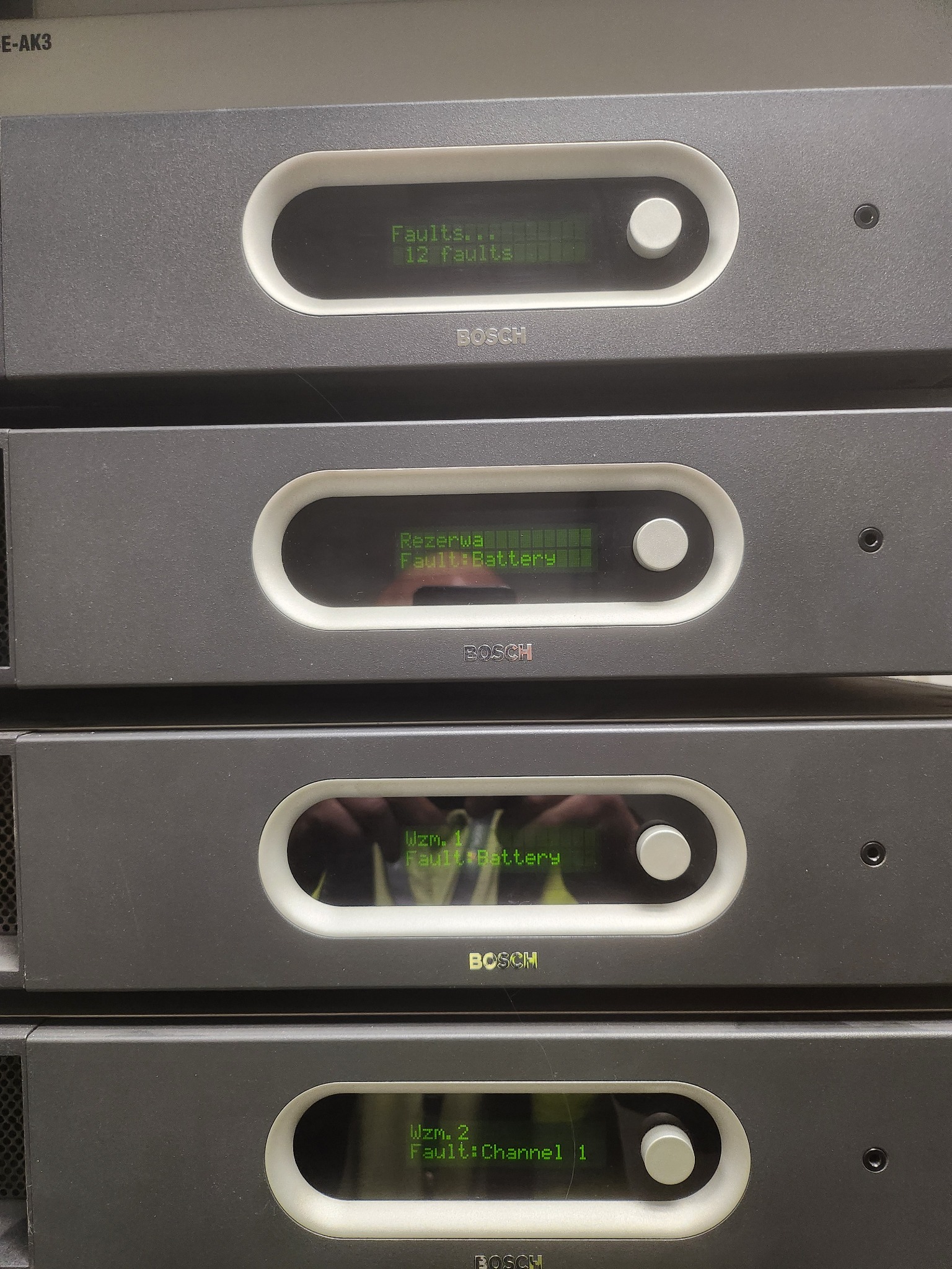 Stos urządzeń Bosch z wyświetlaczami wskazującymi błędy: 12 faults, Fault Battery, Fault Channel 1. Szara obudowa, białe obramowania wyświetlaczy.