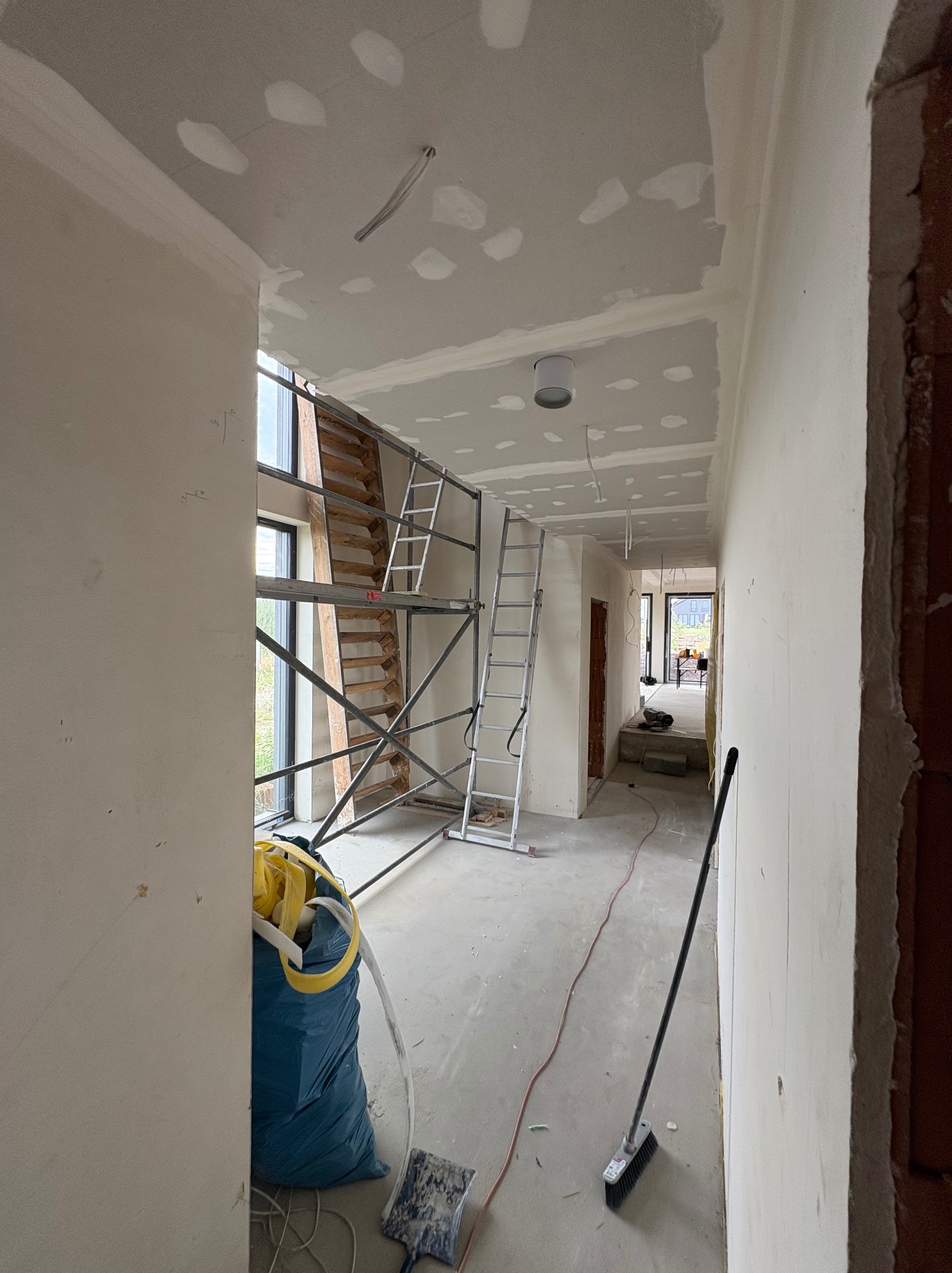 Wnętrze w trakcie prac wykończeniowych: szpachlowane ściany i sufit, rusztowania, narzędzia. Widoczny etap przygotowania do malowania w nowym domu.