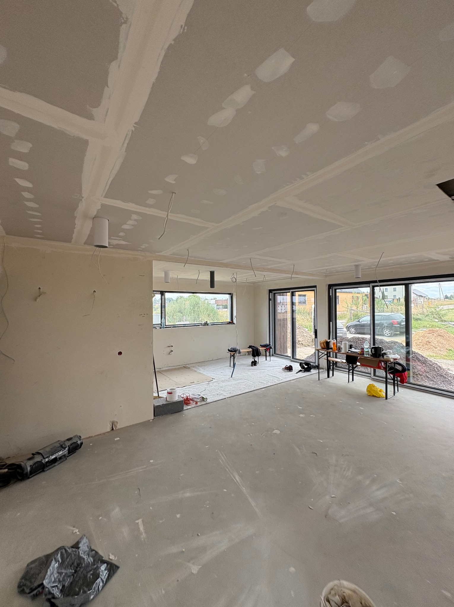 Wnętrze w trakcie prac z płyt karton-gips w Gliwicach. Widoczne łączenia płyt na suficie, przygotowane do szpachlowania. Surowy beton na podłodze, duże okna.