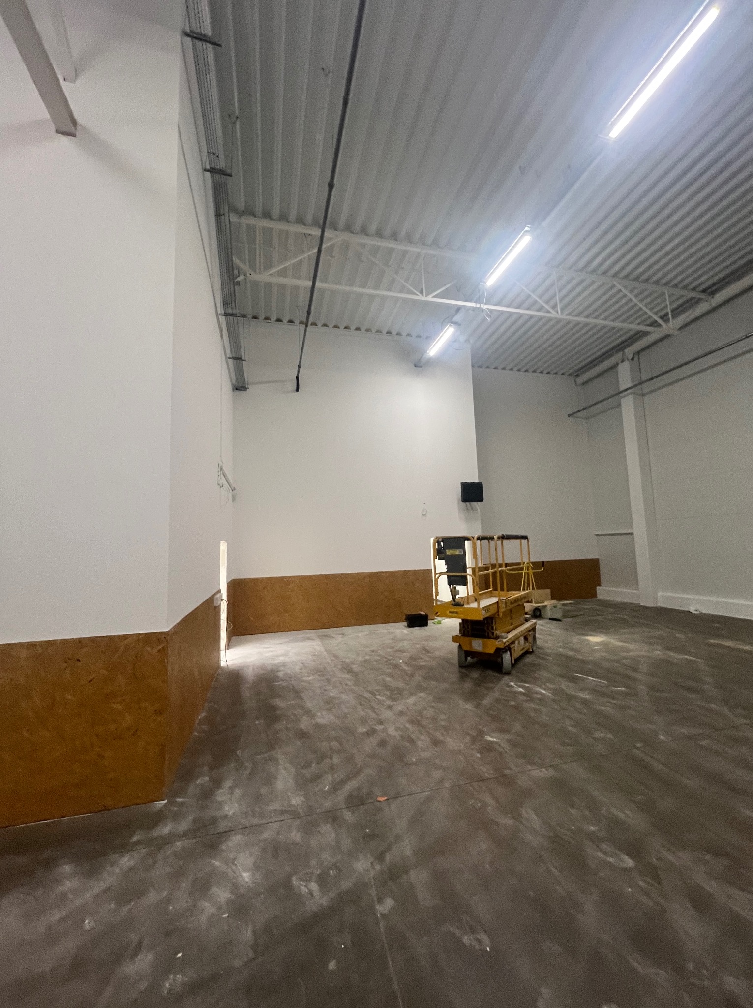 Wnętrze hali przemysłowej po remoncie, z podnośnikiem nożycowym na środku. Ściany pomalowane na biało, z brązowym pasem na dole. Widoczna instalacja pod sufitem.