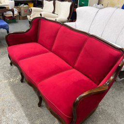 Zakład tapicerski VIOLA - Czerwona, odrestaurowana sofa w stylu retro z drewnianymi zdobieniami. Usługi tapicerskie w Jasin. Widoczne inne meble w tle.