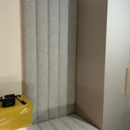 Tapicerowany, szary panel ścienny z siedziskiem w zabudowie meblowej. Widoczny narzędzia tapicerskie. Nowoczesny design, tekstylna faktura.