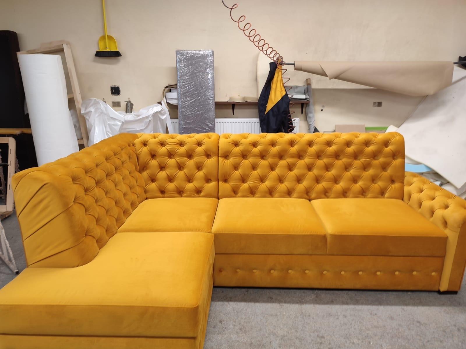 Żółta, pikowana sofa narożna z weluru w warsztacie tapicerskim. Widoczne narzędzia i materiały w tle. Detal wykończenia i kolorystyka mebla.