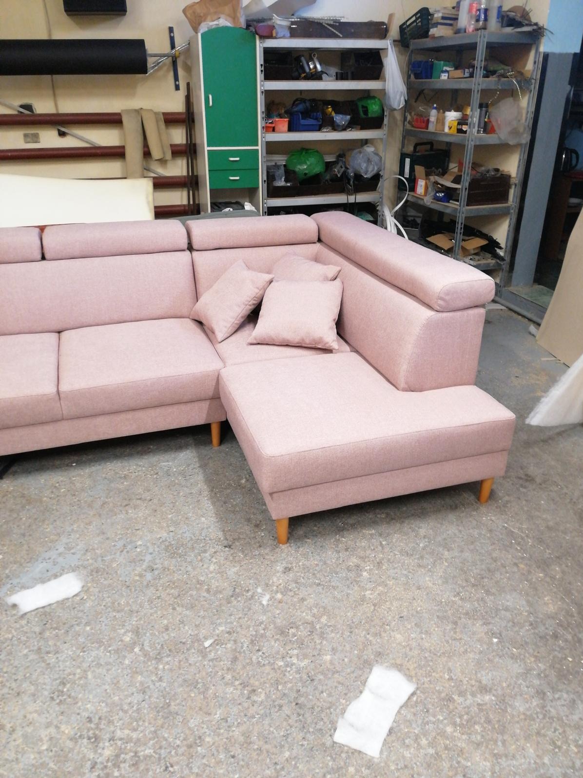 Różowa sofa narożna z poduszkami w warsztacie, widoczna na tle regałów z narzędziami, ukazana w neutralnym oświetleniu.
