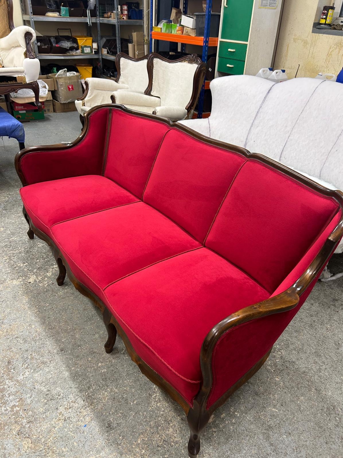 Czerwona, odrestaurowana sofa w stylu retro z drewnianymi zdobieniami. Usługi tapicerskie w Jasin. Widoczne inne meble w tle.