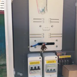 Skrzynka elektryczna w trakcie montażu: widoczne zabezpieczenia przedlicznikowe, rozłącznik zalicznikowy, przewody. Detal: miejsce dostarczania energii, granica własności.