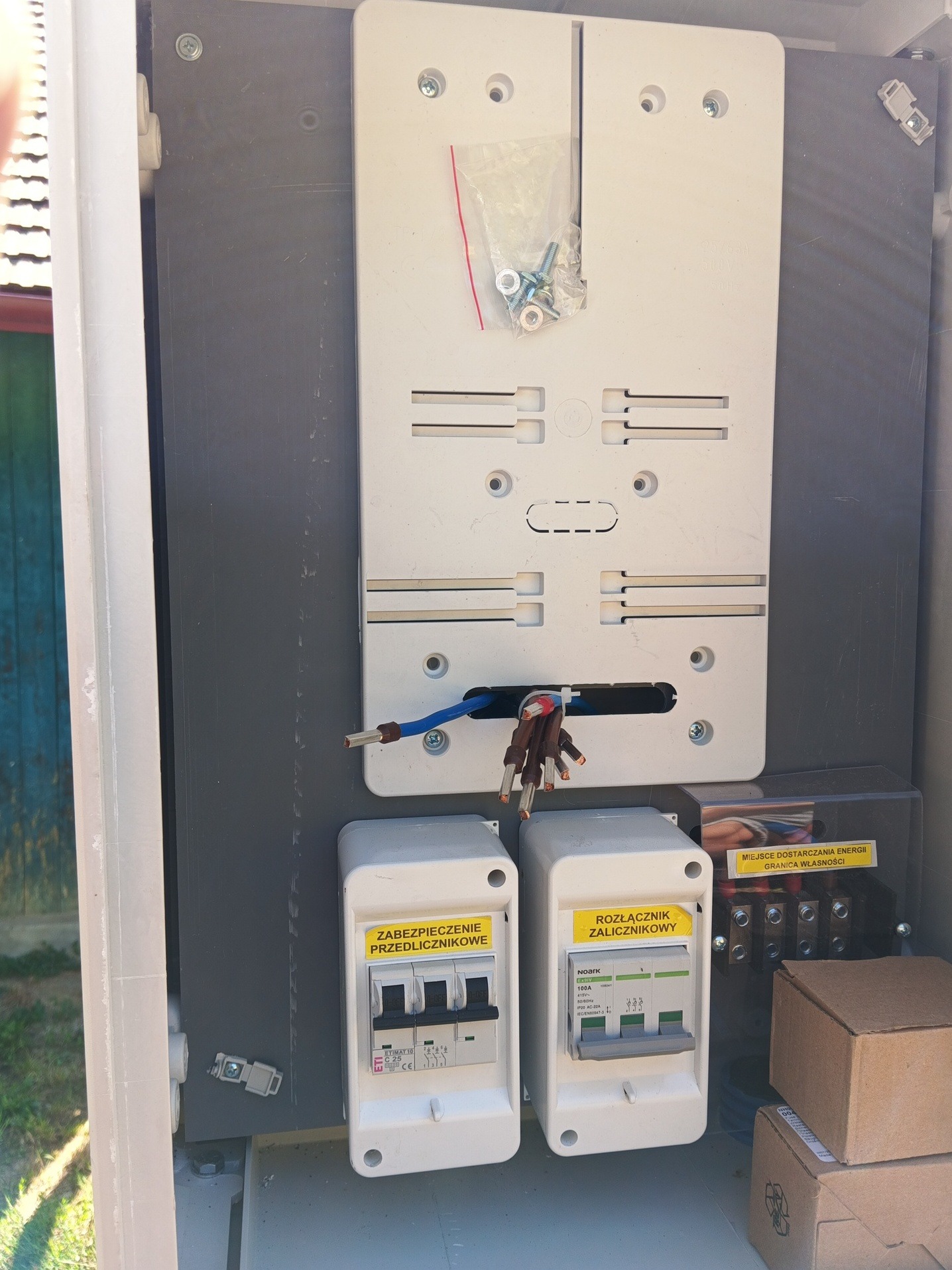 Skrzynka elektryczna w trakcie montażu: widoczne zabezpieczenia przedlicznikowe, rozłącznik zalicznikowy, przewody. Detal: miejsce dostarczania energii, granica własności.
