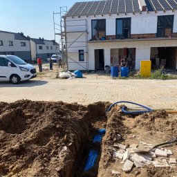ELEKTRO-TOM - Wykop z niebieskimi rurami w ziemi na tle budowy domu w zabudowie szeregowej. Widoczni pracownicy i samochód dostawczy.