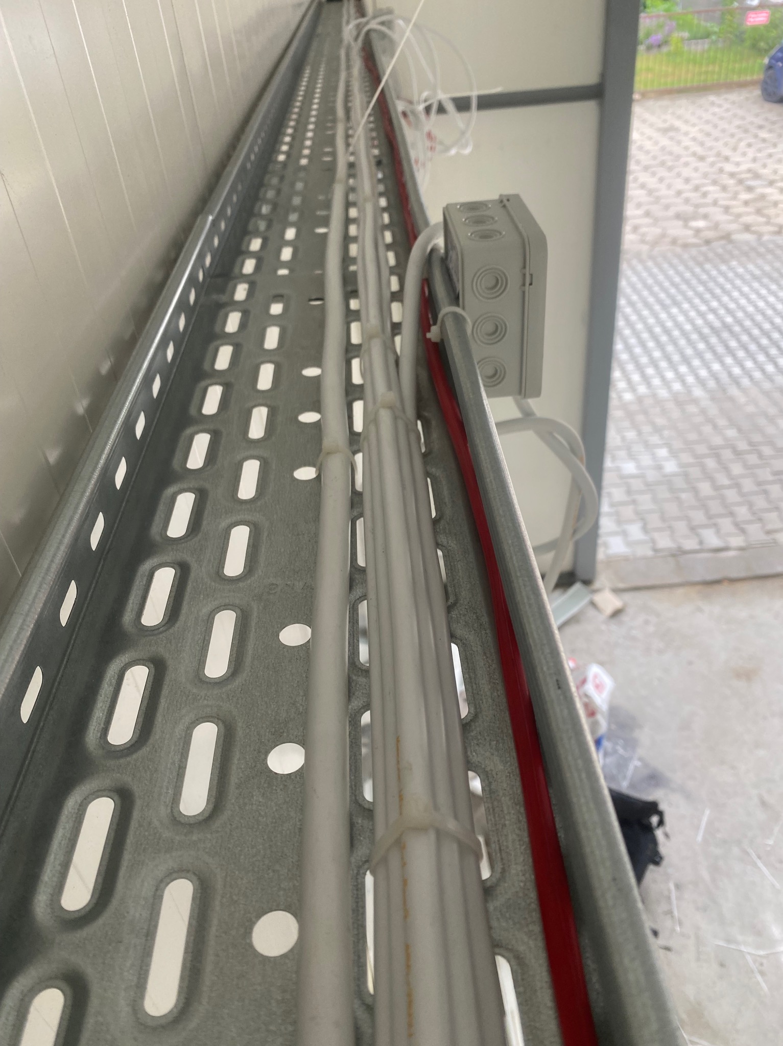 Szyna kablowa z przewodami w budynku. Widoczna puszka instalacyjna i kable prowadzone wzdłuż ściany. Ujęcie z dołu, perspektywa zbieżna.