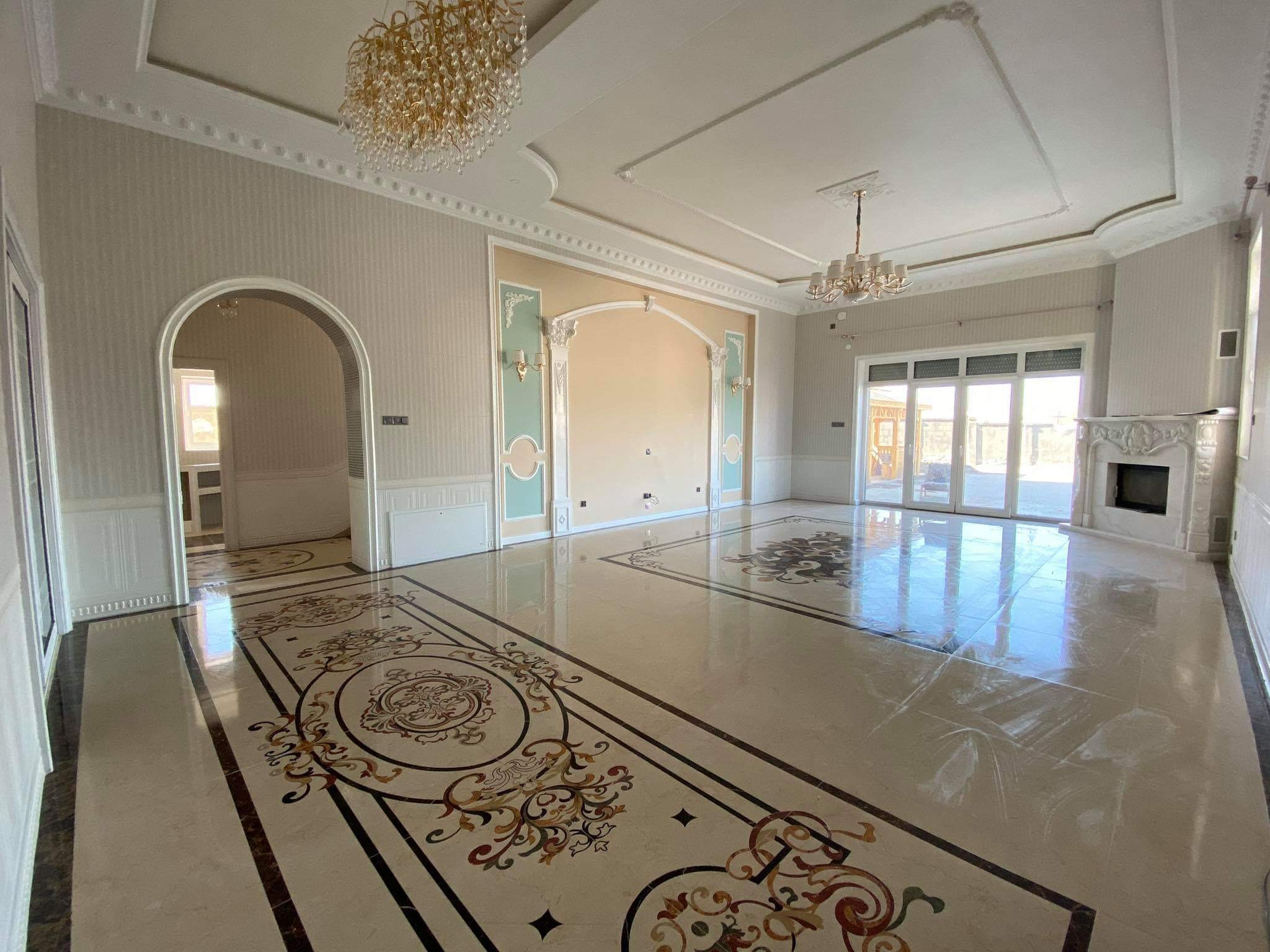 Eleganckie wnętrze po remoncie: błyszcząca podłoga z dekoracyjnymi wzorami, kremowe ściany z dekoracyjnymi elementami i kryształowe żyrandole.