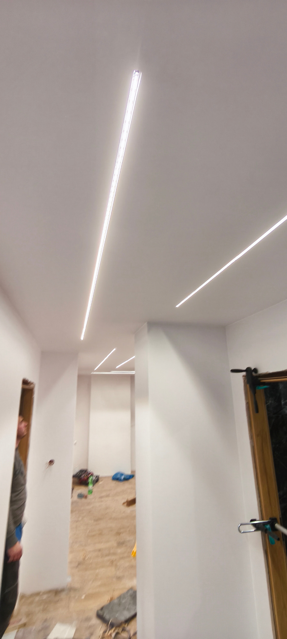 Nowoczesne oświetlenie LED wpuszczone w sufit w jasnym wnętrzu. Widoczne fragmenty pomieszczeń z przygotowaniem do dalszych prac wykończeniowych.