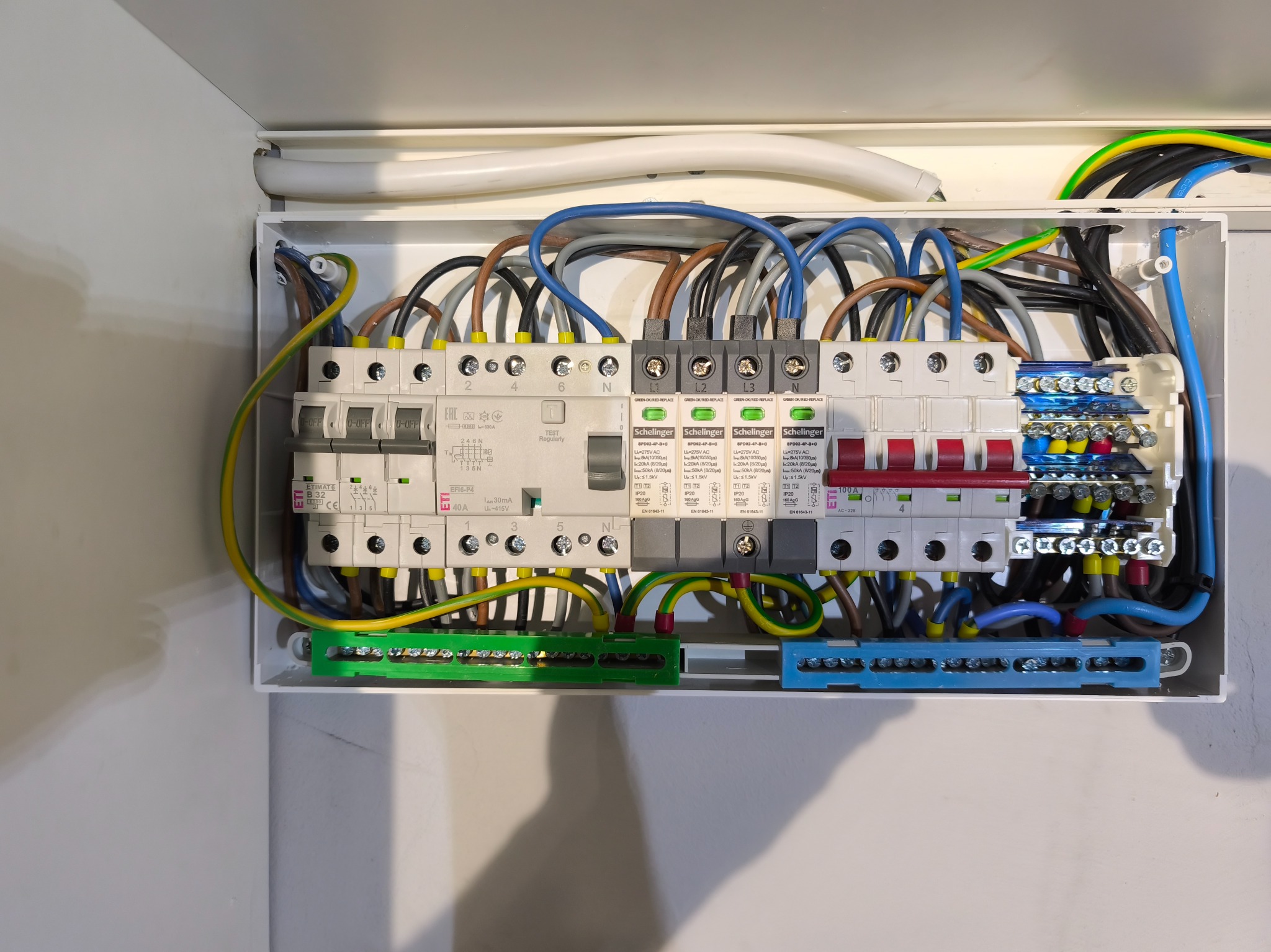 Rozdzielnica elektryczna z zainstalowanymi bezpiecznikami, przewodami w różnych kolorach i listwami zaciskowymi. Widoczne elementy marki Schellinger i ETI.