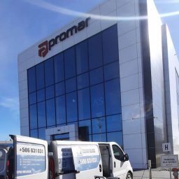 Clean Glass Professional - Nowoczesny biurowiec Promar z dużymi, czystymi oknami, odbijającymi niebo. Na pierwszym planie samochody Clean Glass z numerem telefonu i logo firmy.