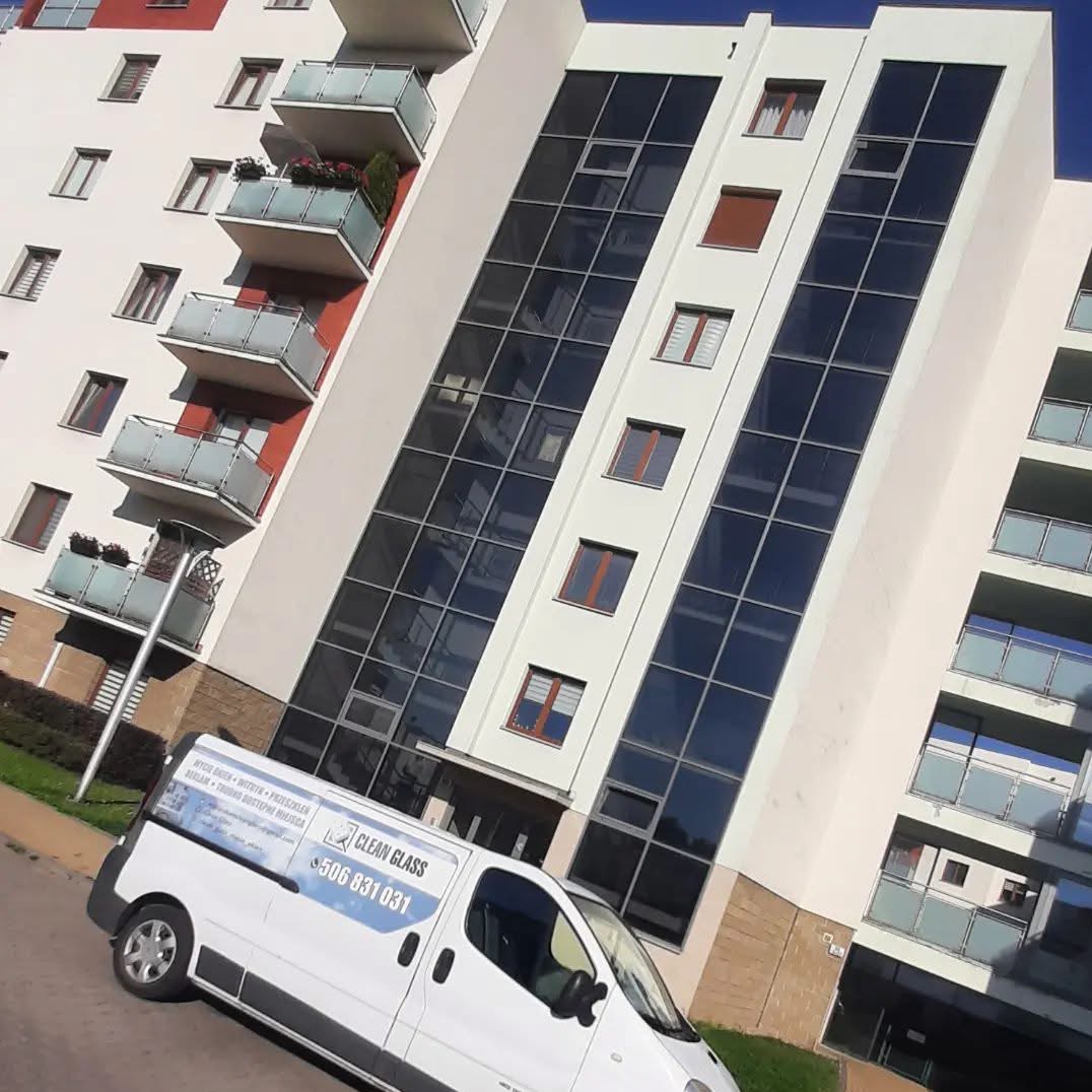 Biały budynek z balkonami i dużymi oknami, na tle zaparkowany biały van z logo firmy oferującej mycie okien. Budynek po umyciu okien.