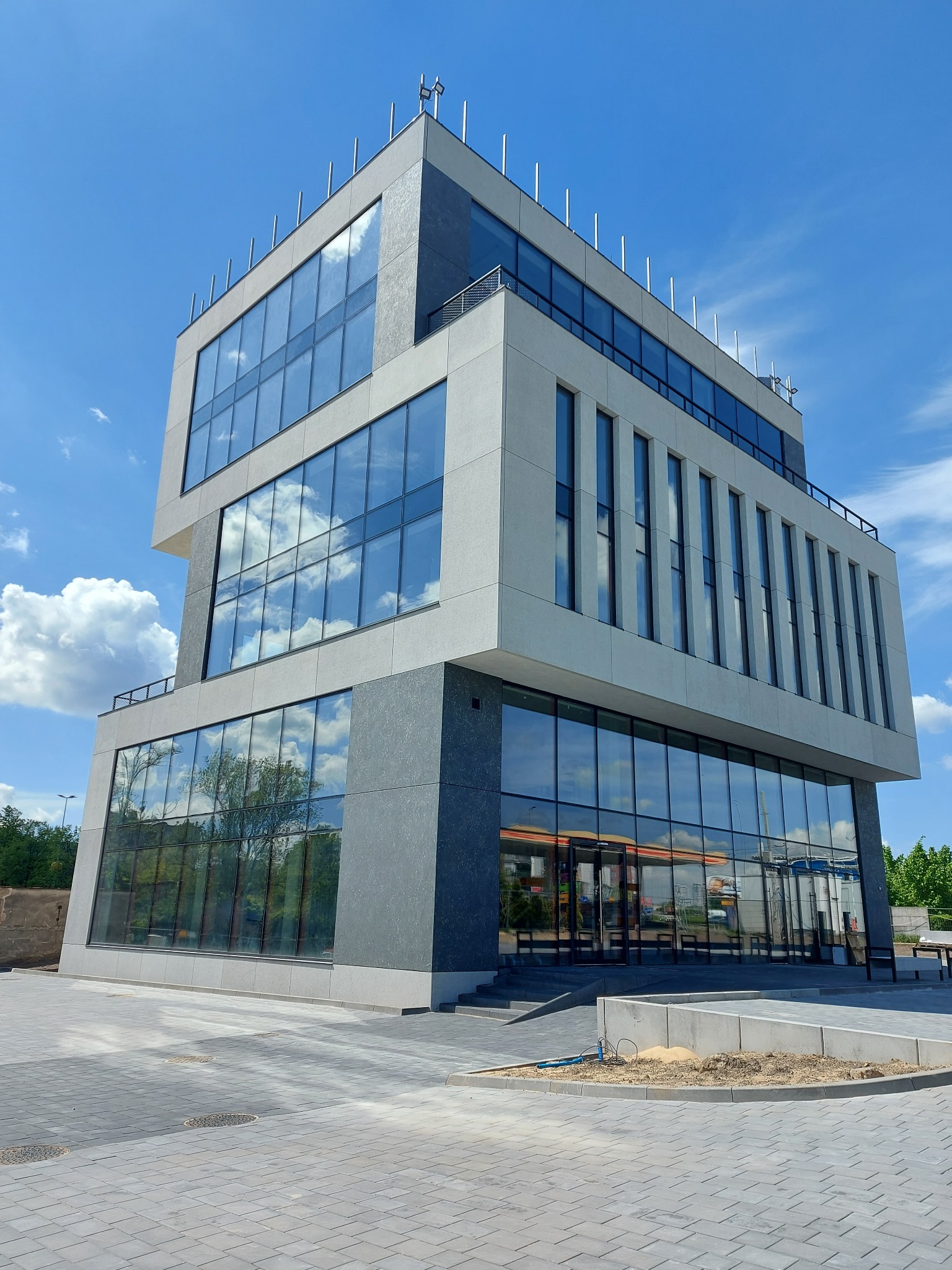 Nowoczesny, trzypiętrowy budynek biurowy z dużymi oknami, w których odbija się błękitne niebo z chmurami. Widok z dołu, podkreślający geometryczną bryłę.