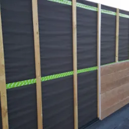 Montaż paneli elewacyjnych na balkonie: widoczne drewniane listwy, czarna membrana i częściowo zamontowane panele w kolorze drewna. W tle drabina i materiały.