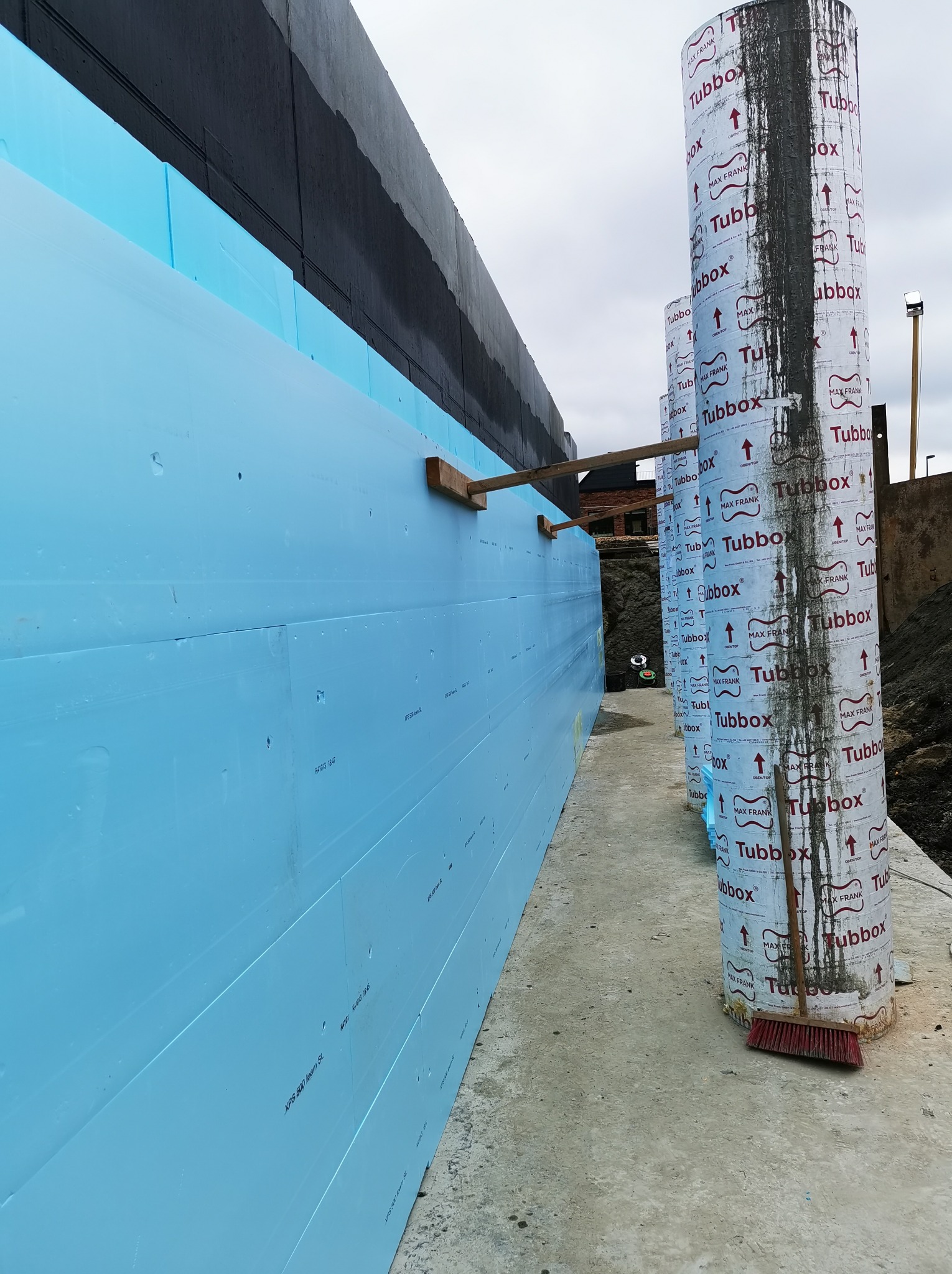 Izolacja fundamentu z niebieskiego styropianu XPS i szalunki Tubbox przed betonowaniem. Widok na plac budowy z narzędziami.