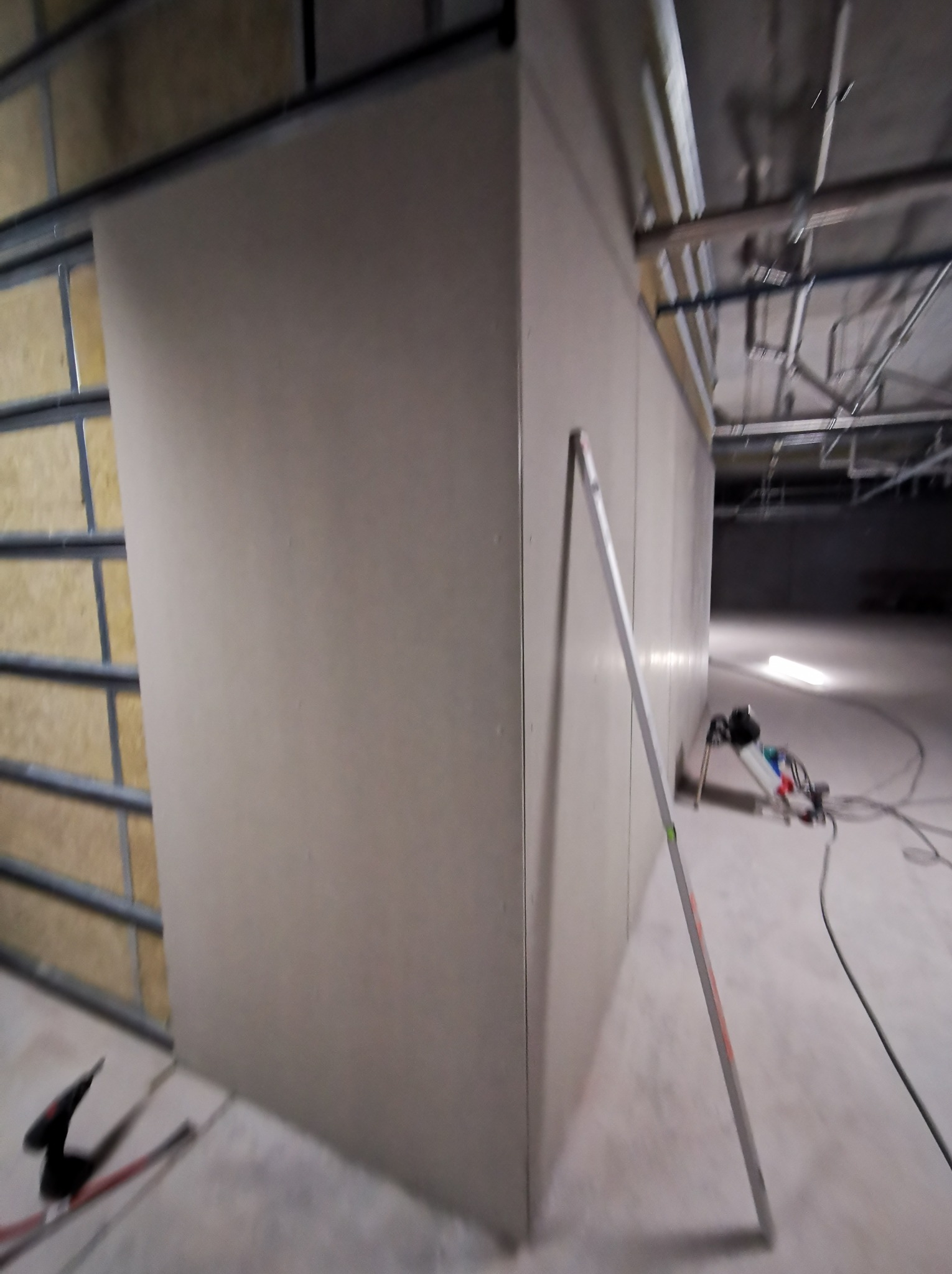 Montaż ścian działowych z płyt gipsowo-kartonowych na metalowym stelażu w przestrzeni komercyjnej. Widoczna poziomica i narzędzia.