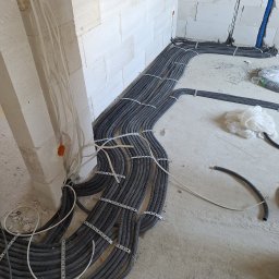 Adam Remontuje - Instalacja elektryczna w peszlach, mocowana do ściany z betonu komórkowego. Widoczne kable w ścianie i na podłodze w surowym stanie.