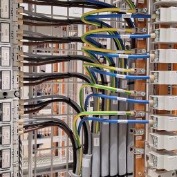 Adam Remontuje - Szczegółowe ujęcie na profesjonalnie ułożone kable w szynie montażowej, z precyzyjnym oznaczeniem i uporządkowanym prowadzeniem przewodów. Widoczne elementy instalacji elektrycznej.