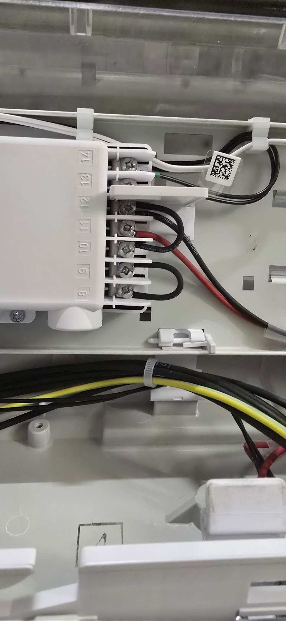 Wnętrze puszki elektrycznej z podłączonymi przewodami o różnych kolorach, w tym czarnym, czerwonym i żółto-zielonym. Widoczne złącza śrubowe i oznaczenia numerów na listwie.