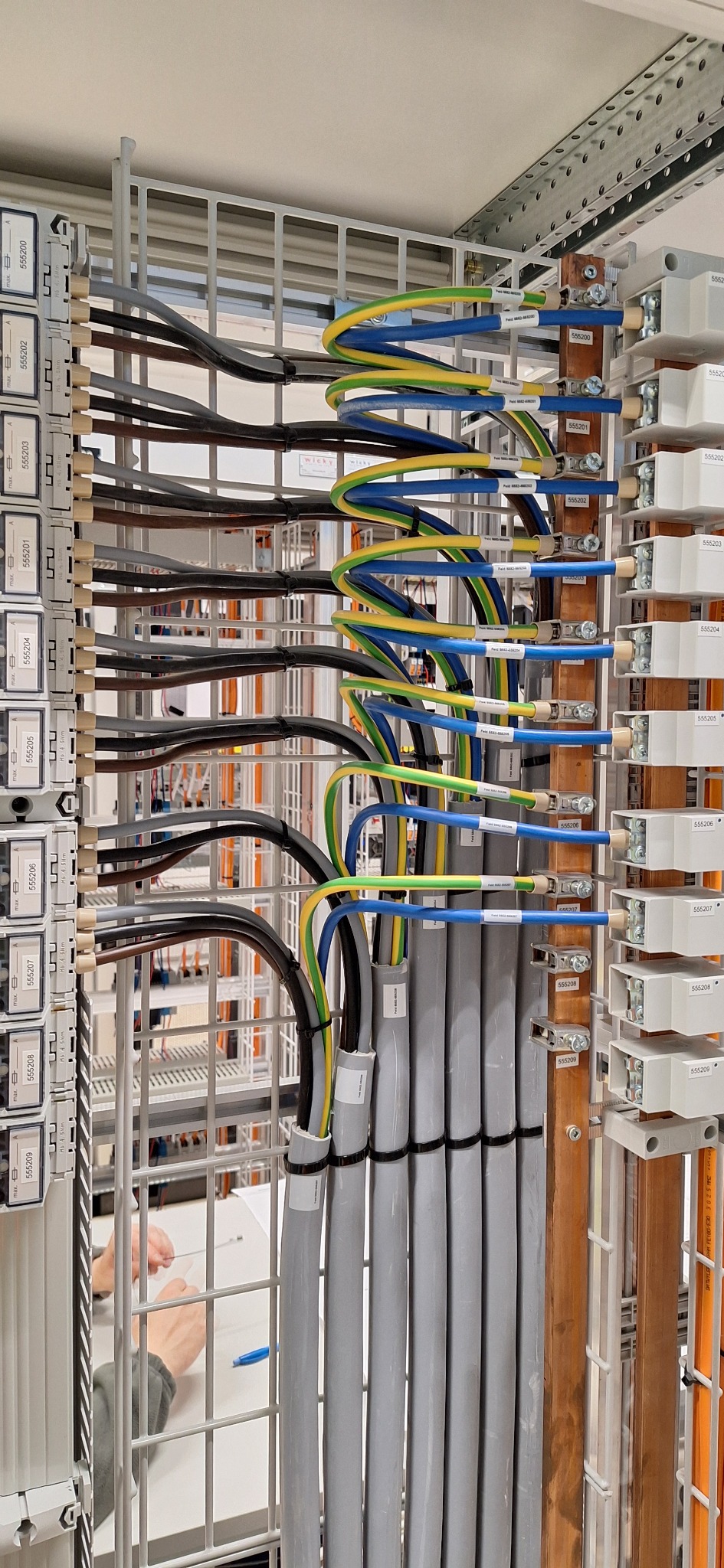Szczegółowe ujęcie na profesjonalnie ułożone kable w szynie montażowej, z precyzyjnym oznaczeniem i uporządkowanym prowadzeniem przewodów. Widoczne elementy instalacji elektrycznej.