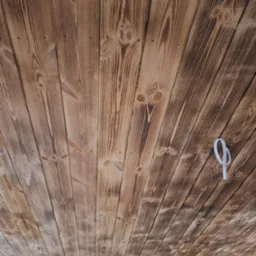 Wykończony drewniany sufit z widocznymi śladami po przypalaniu, ułożony z desek pod kątem. Widoczne mocowania i fragment ściany z cegły.