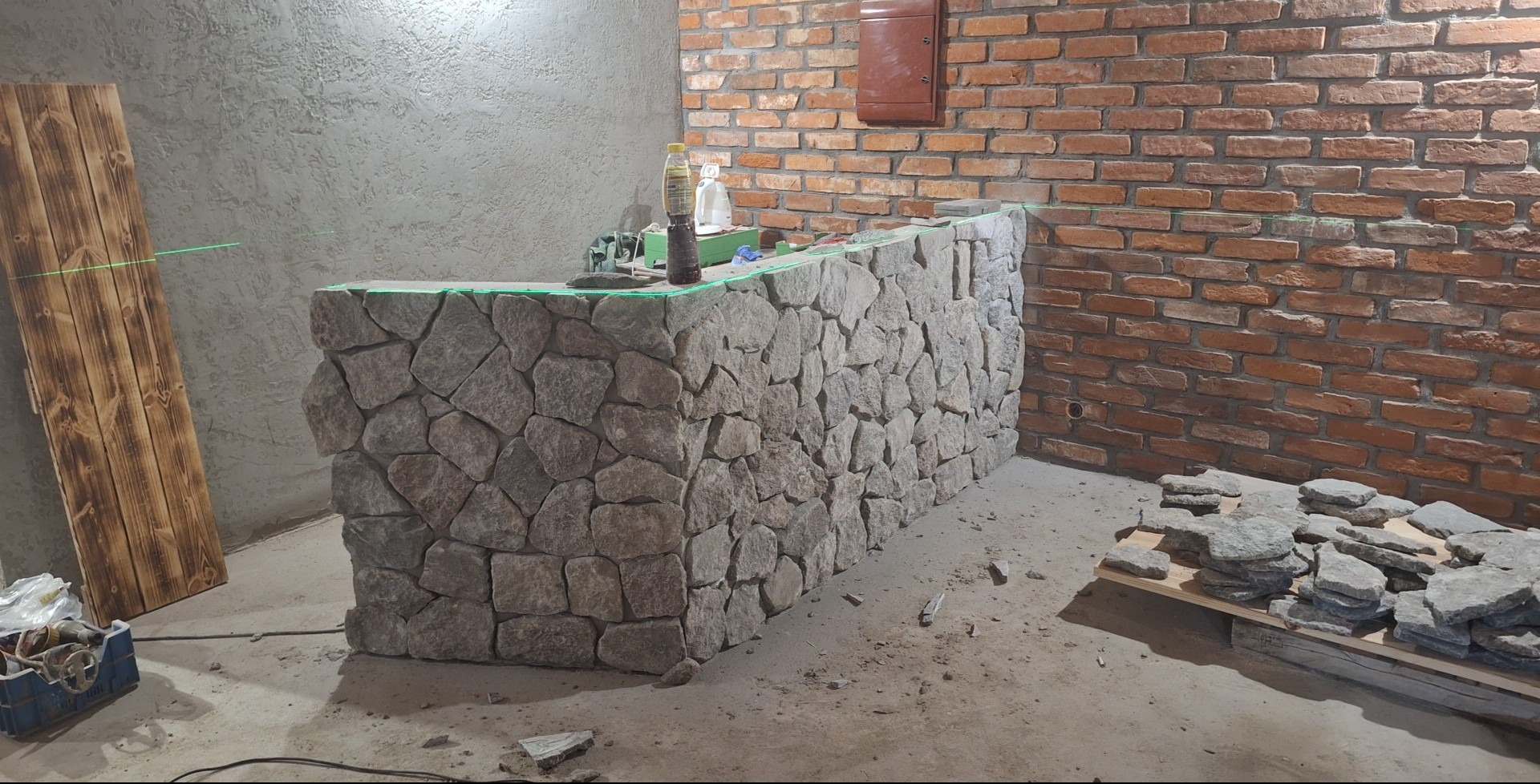 Bar z kamienia naturalnego w trakcie montażu, poziomica laserowa, surowa ściana z cegły i tynk. Elementy wykończenia wnętrz w stylu rustykalnym.